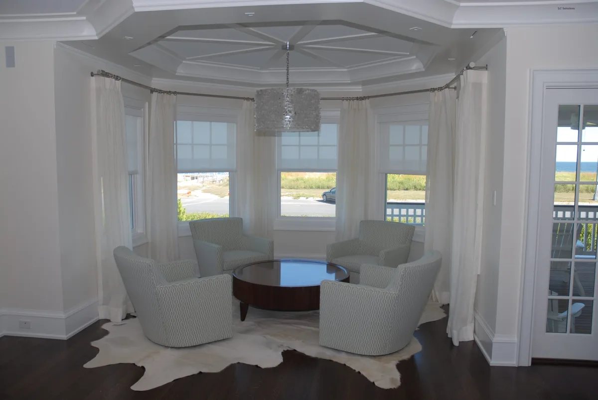Solar roller shades with drapery side panels on custom bay hardware in a Spring Lake home